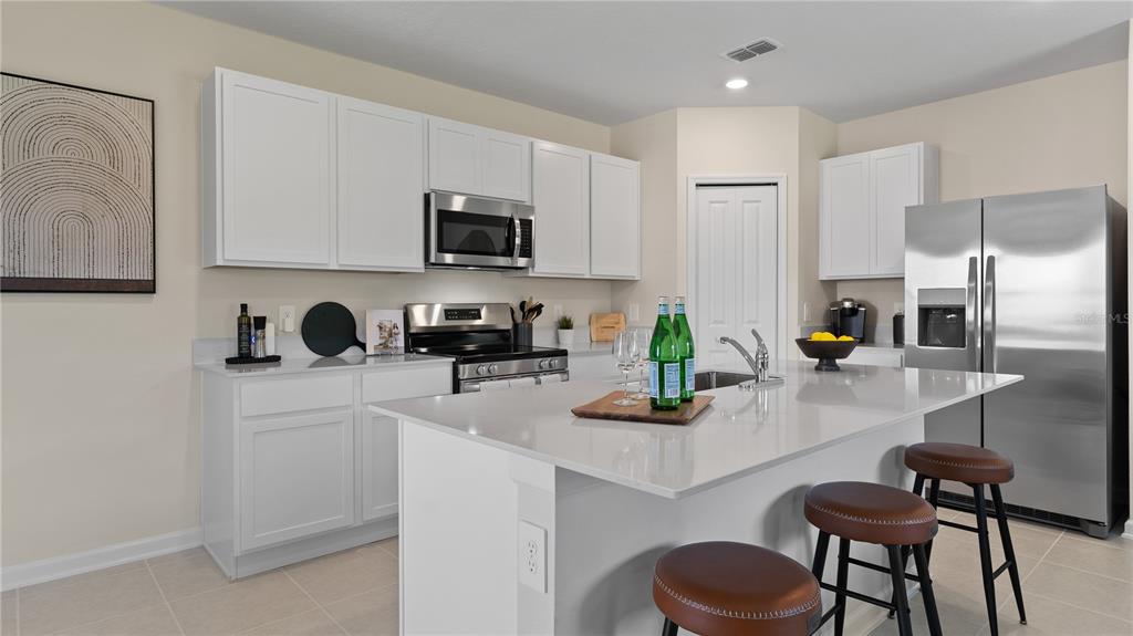 A modern kitchen features white cabinetry, stainless steel appliances, and a large quartz-topped island — 6253 BOTTICELLA BOULEVARD, WINTER HAVEN, FL
