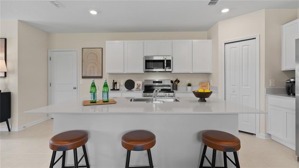 A kitchen features a white island with three stools, white cabinetry, and stainless steel appliances — 6253 BOTTICELLA BOULEVARD, WINTER HAVEN, FL