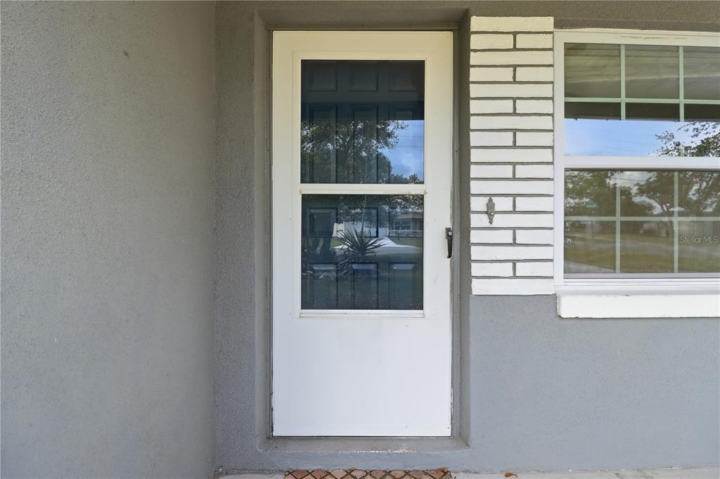 A white storm door is mounted on a gray exterior wall next to a window — 38 REGINA BOULEVARD, BEVERLY HILLS, FL