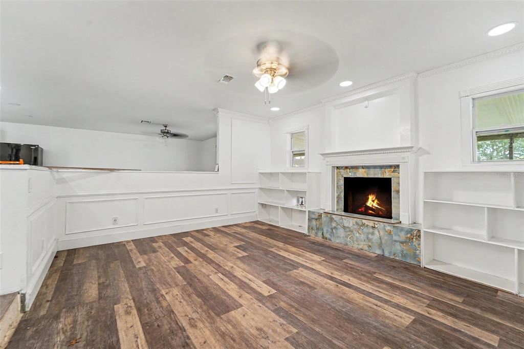 A living room features wood-look flooring, white wainscoting, built-in shelving, and a marble-tiled fireplace — 10938 SALT TREE DRIVE, PORT RICHEY, FL