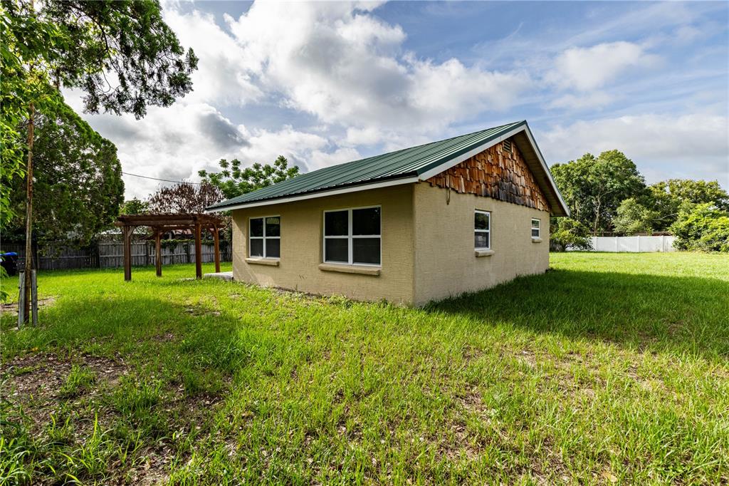 A small, tan-colored house with a green metal roof sits in a grassy yard — 7020 SCOTT AVENUE, MOUNT DORA, FL