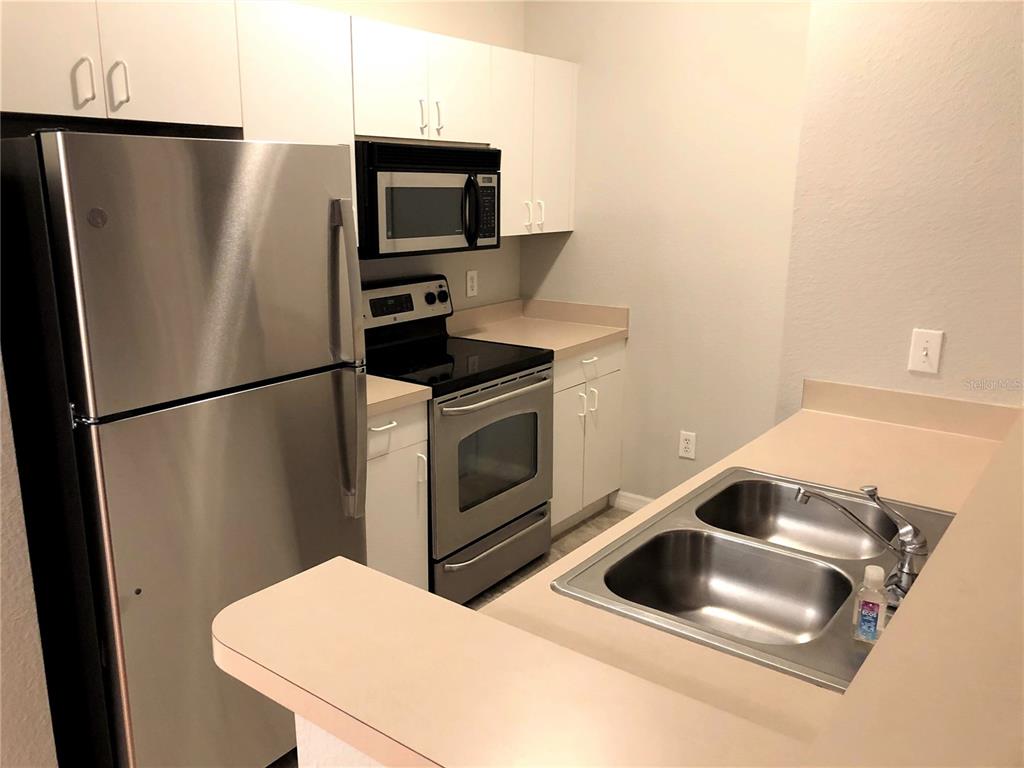 A kitchen features stainless steel appliances, white cabinetry, and a double-basin sink — 3725 CONROY ROAD UNIT 2113, ORLANDO, FL