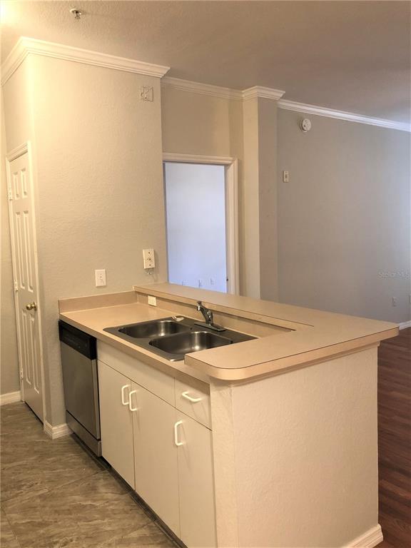 A kitchen island with a double sink, dishwasher, and beige countertops faces an open room — 3725 CONROY ROAD UNIT 2113, ORLANDO, FL