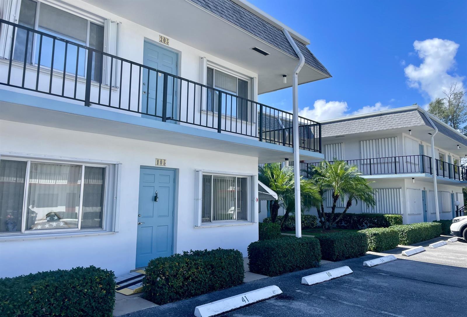 A two-story white apartment building features blue doors, black railings, and a parking lot — 2880 Lake Osborne Drive # 205, FL 33461, FL