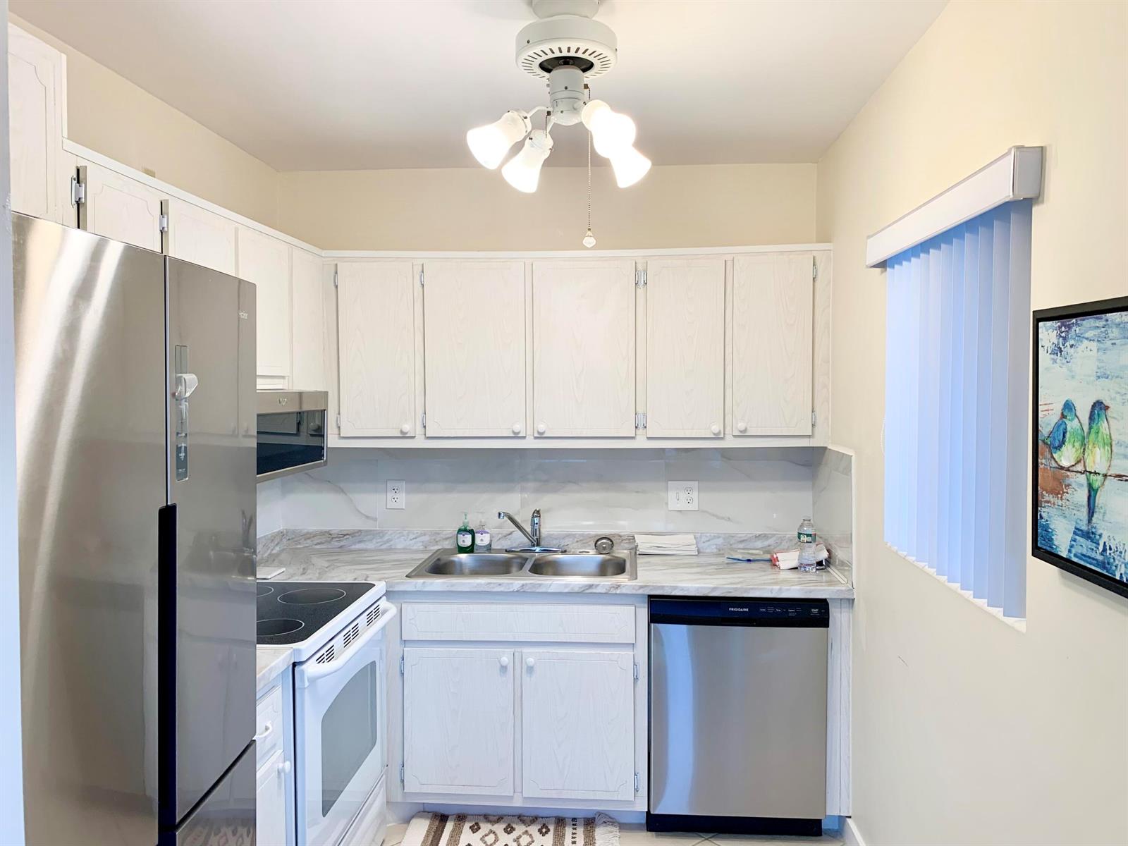 A kitchen with white cabinets, stainless steel appliances, marble-look countertops, and a ceiling fan light — 2880 Lake Osborne Drive # 205, FL 33461, FL