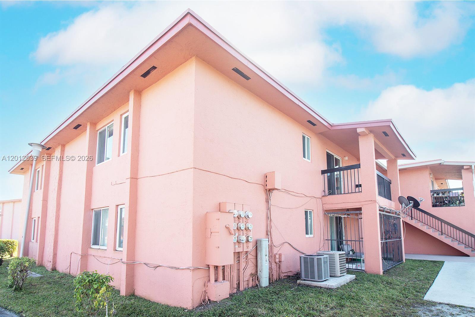 A two-story pink stucco apartment building features exterior staircases and multiple electrical meter boxes — 2020 NW 119th St # 1121, Miami FL 33167, MIAMI, FL