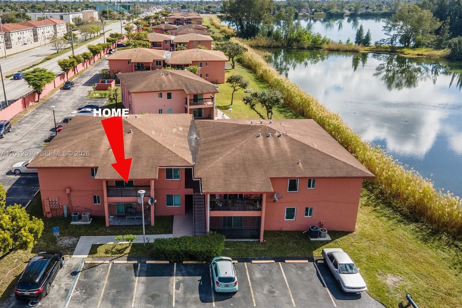An aerial view shows a multi-story peach-colored apartment building next to a lake — 2020 NW 119th St # 1121, Miami FL 33167, MIAMI, FL