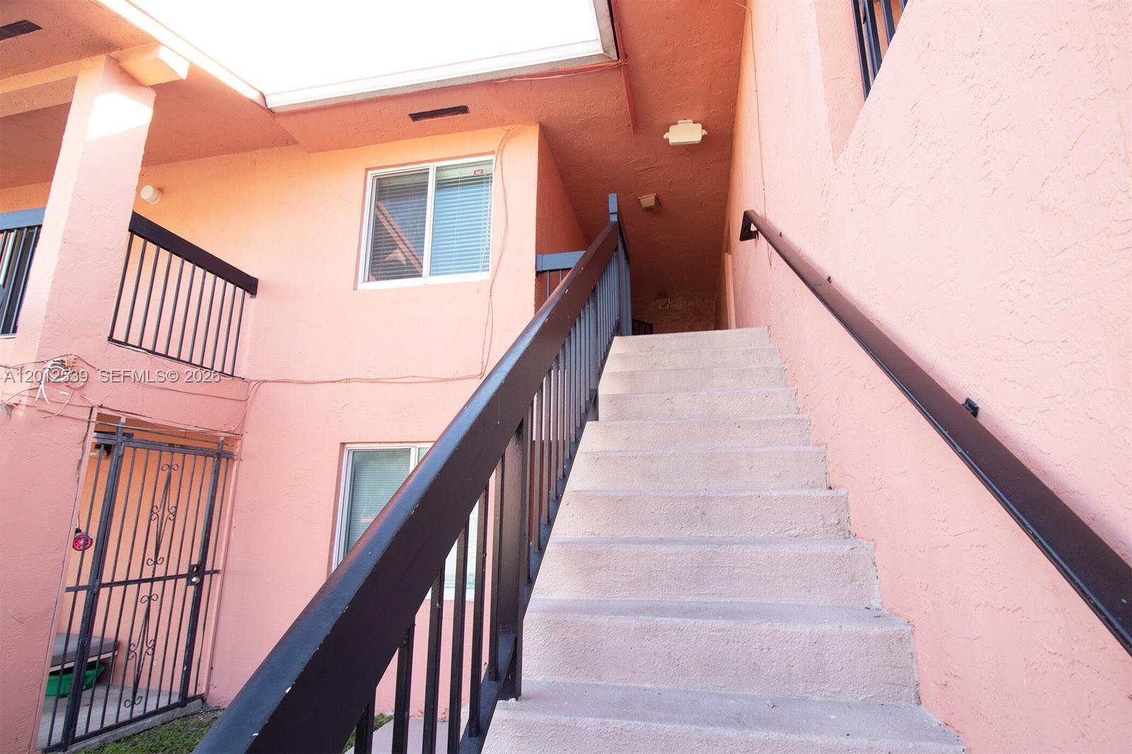 An exterior view shows a pink building with a concrete staircase leading to an upper level — 2020 NW 119th St # 1121, Miami FL 33167, MIAMI, FL