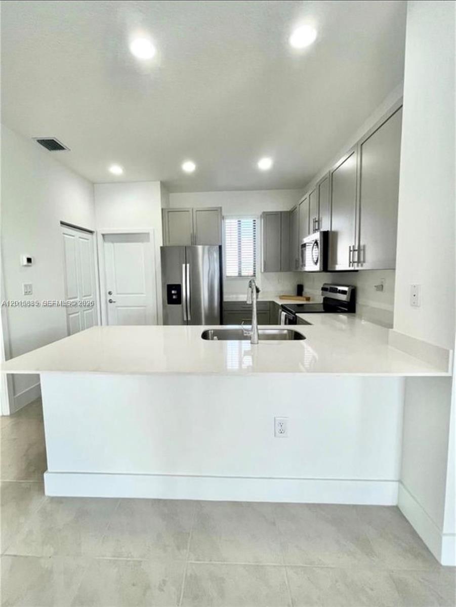 A modern kitchen features gray cabinets, stainless steel appliances, and a white quartz breakfast bar — 4982 Brigata Way, Ave Maria FL 34142, AVE MARIA, FL