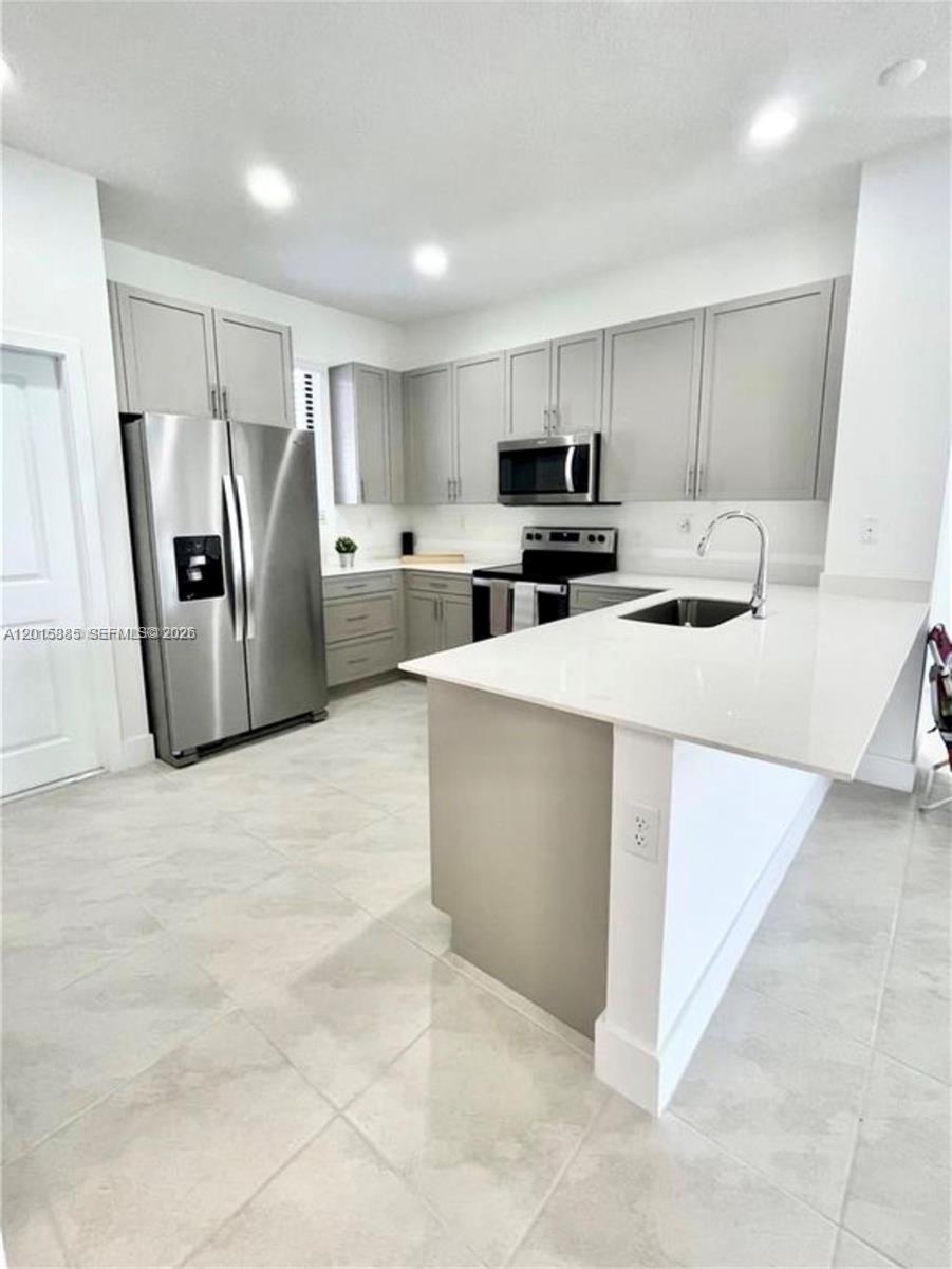 A modern kitchen features gray cabinets, stainless steel appliances, and a white quartz peninsula — 4982 Brigata Way, Ave Maria FL 34142, AVE MARIA, FL