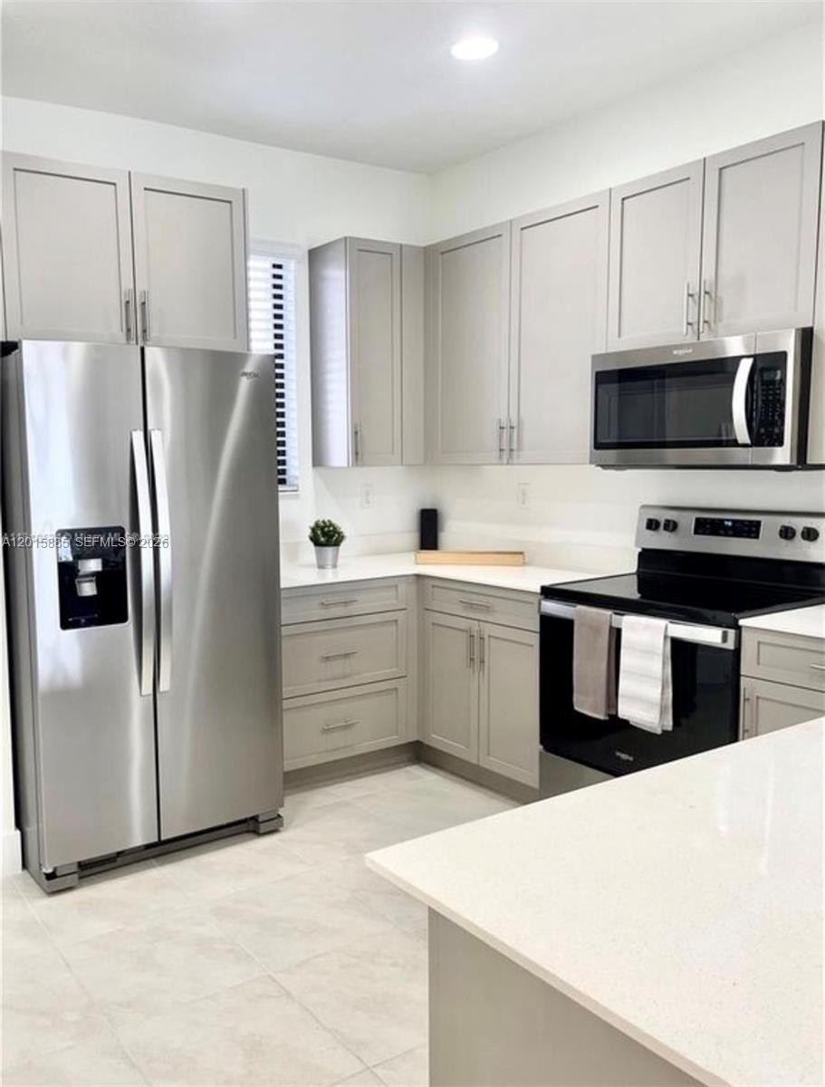 A modern kitchen features light gray cabinets, stainless steel appliances, and white quartz countertops — 4982 Brigata Way, Ave Maria FL 34142, AVE MARIA, FL