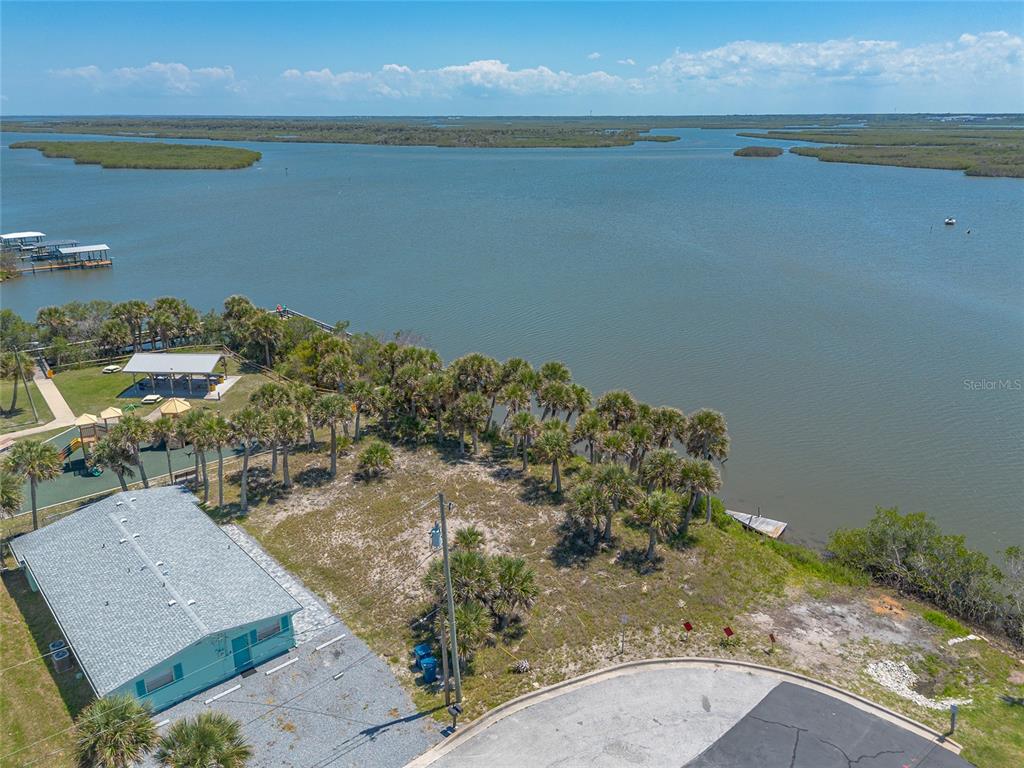 An aerial view shows a house, a playground, and palm trees bordering a large body of water — 0 LADYFISH AVENUE, NEW SMYRNA BEACH, FL