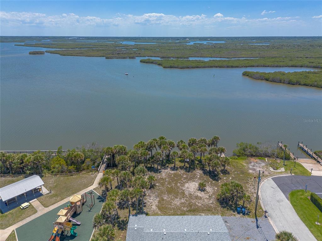 An aerial view shows a playground, palm trees, and a dock along a large body of water — 0 LADYFISH AVENUE, NEW SMYRNA BEACH, FL