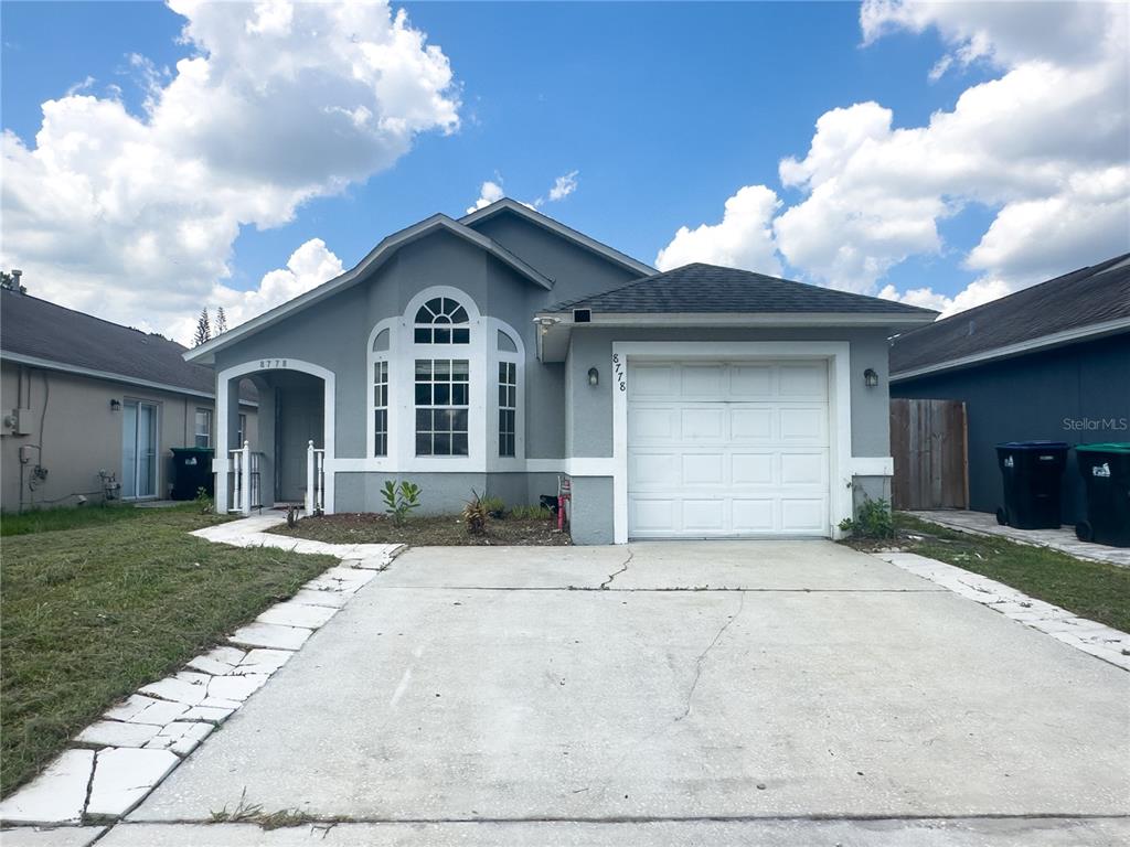 A single-story gray house features a white garage door, a front porch, and a driveway — 8778 FOLEY DRIVE, ORLANDO, FL