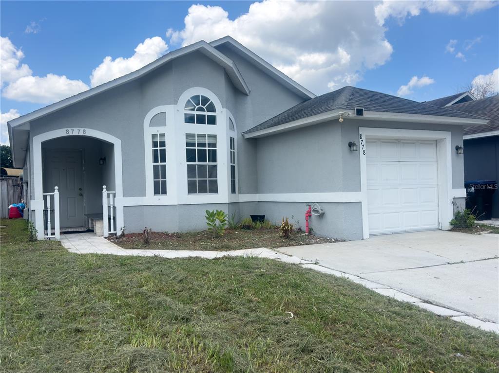 A single-story gray house features a white garage door, a front porch, and arched windows — 8778 FOLEY DRIVE, ORLANDO, FL
