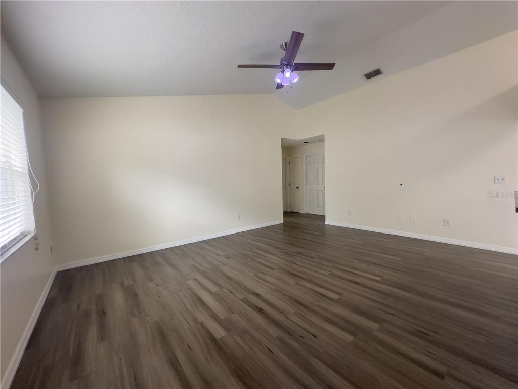 An empty living room features light-colored walls, a ceiling fan, and wood-look laminate flooring — 8778 FOLEY DRIVE, ORLANDO, FL
