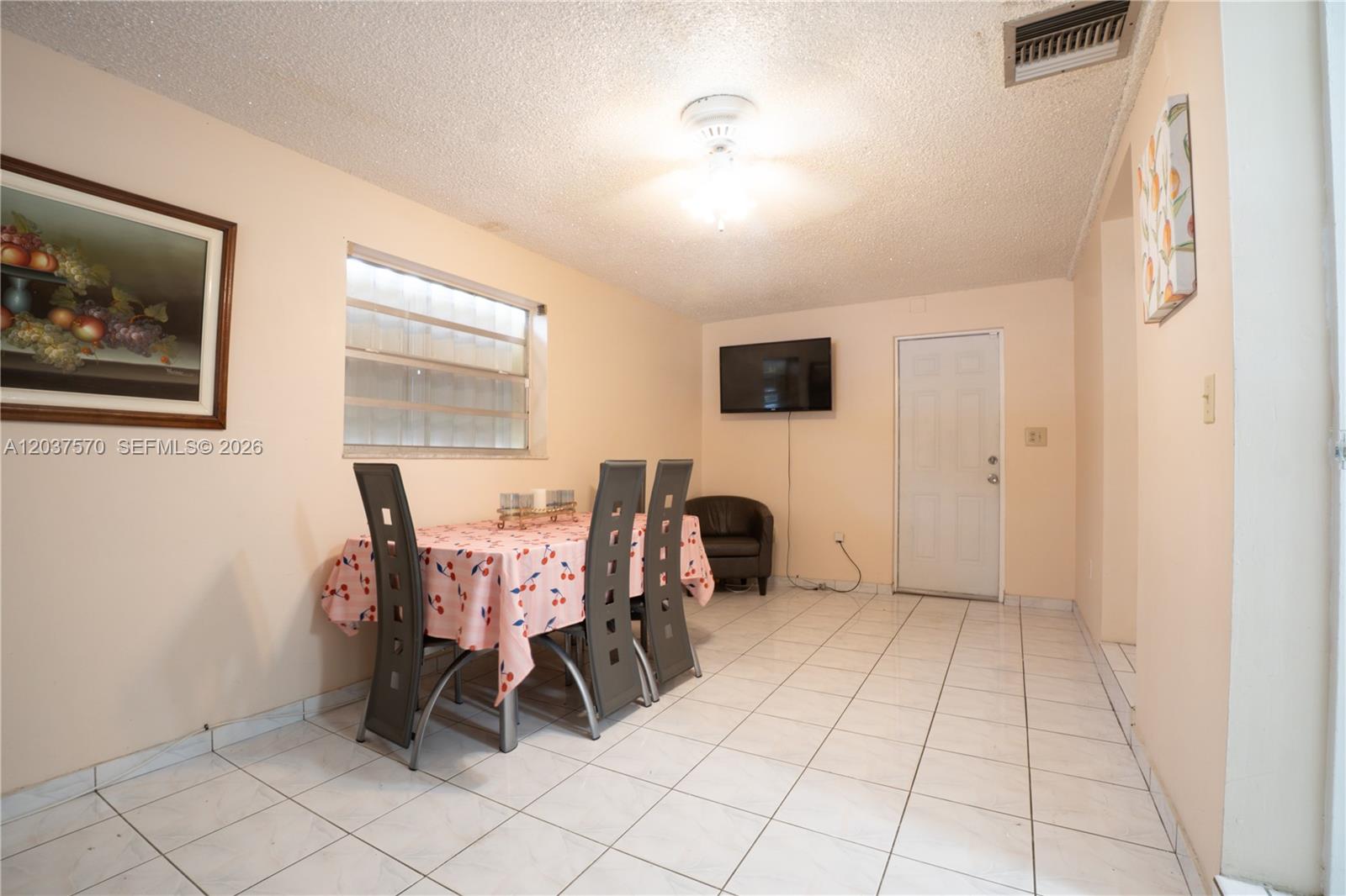 A dining room features a table with a cherry-print tablecloth, tiled floors, and a ceiling fan — 7899 NW 174th Ter, Hialeah FL 33015, HIALEAH, FL