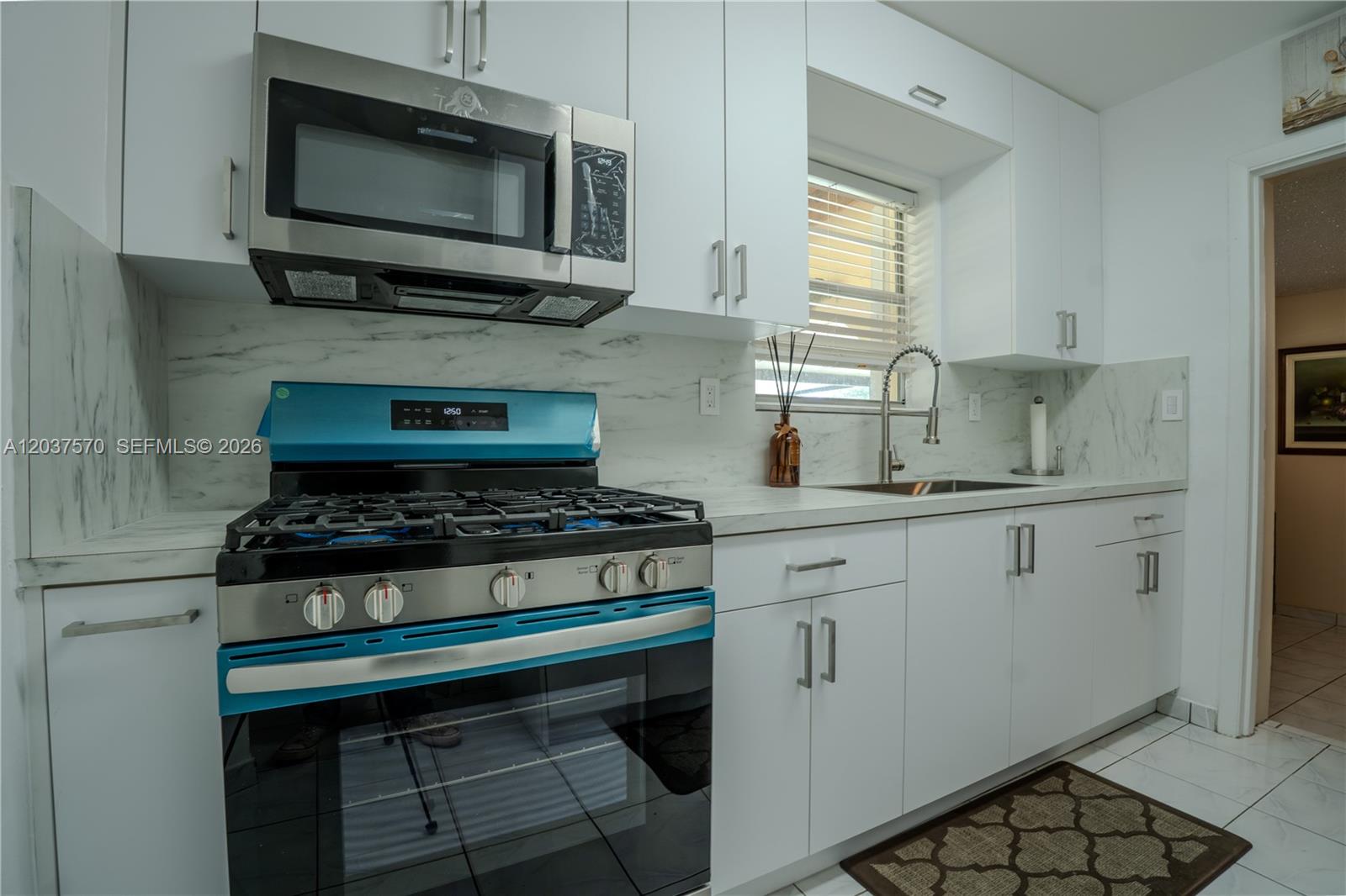 A kitchen features white cabinets, marble-look countertops, a stainless steel microwave, and a blue stove — 7899 NW 174th Ter, Hialeah FL 33015, HIALEAH, FL