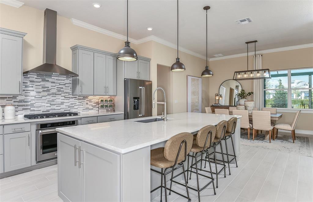 A modern kitchen features gray cabinetry, a large white quartz island, and an adjacent dining area — 6208 SW 82ND TERRACE ROAD, OCALA, FL
