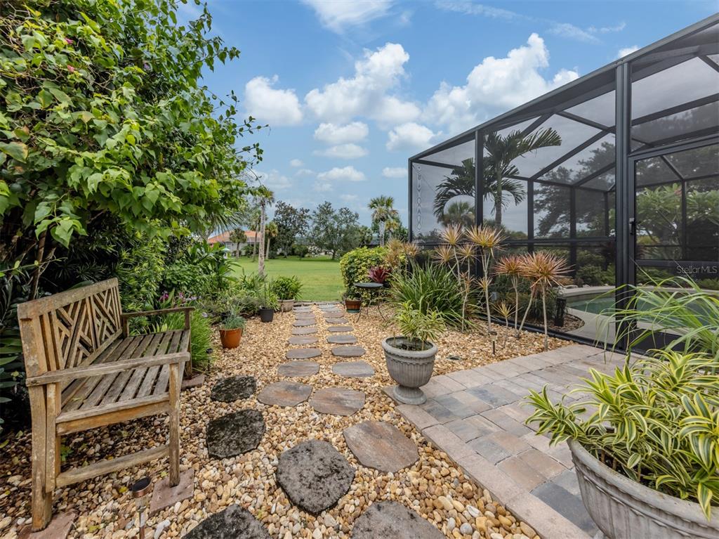 A wooden bench sits on a gravel path beside a screened-in pool enclosure — 151 COCO PALM DRIVE, VENICE, FL
