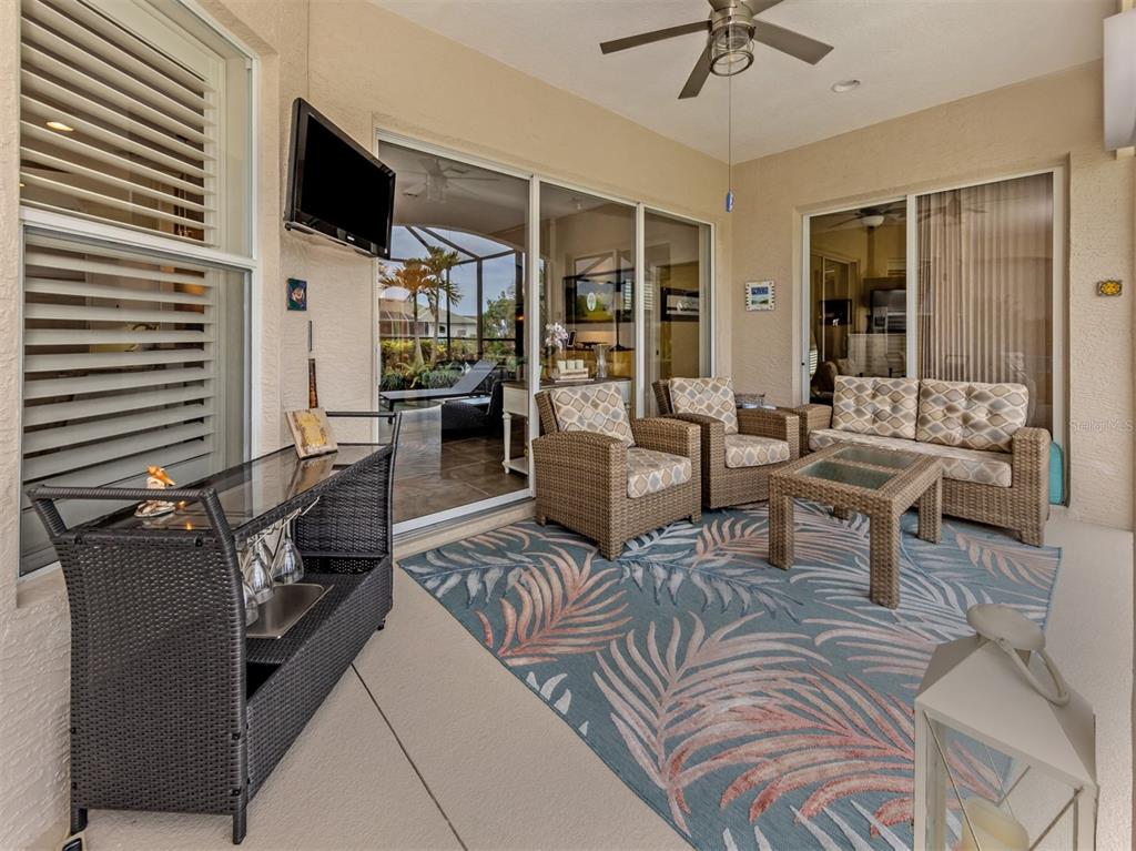 A covered patio features wicker furniture, a patterned area rug, and a wall-mounted television — 151 COCO PALM DRIVE, VENICE, FL