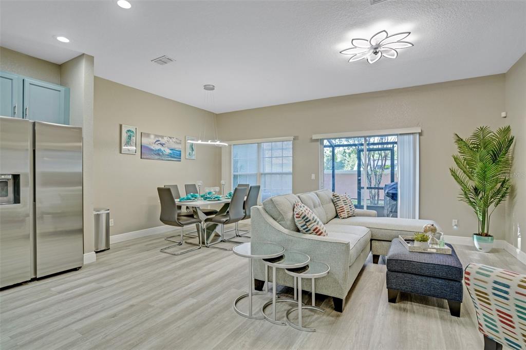 An open-concept living and dining area features light wood-look flooring, a sectional sofa, and stainless appliances — 2468 CARAVELLE CIRCLE, KISSIMMEE, FL
