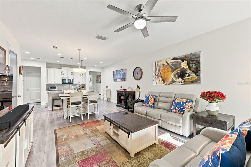 An open-concept living room and kitchen featuring light wood flooring and a ceiling fan — 17815 ALTHEA BLUE PLACE, LUTZ, FL