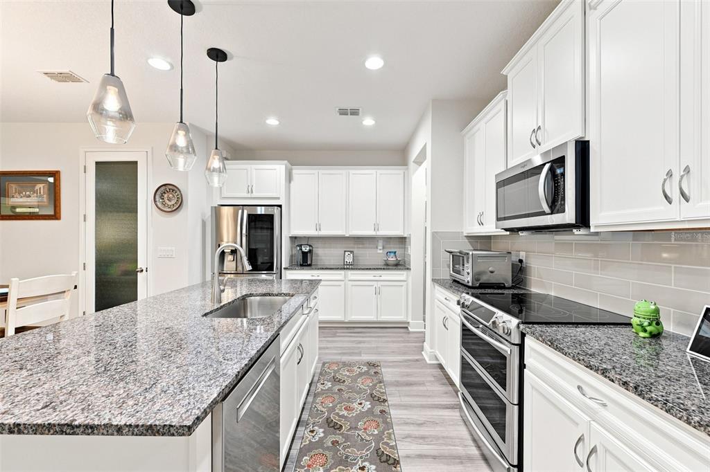 A modern kitchen features white cabinets, granite countertops, stainless steel appliances, and a central island — 17815 ALTHEA BLUE PLACE, LUTZ, FL
