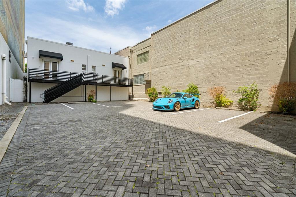 A bright blue sports car is parked in a paved lot beside a white building — 127 N MAGNOLIA AVENUE, ORLANDO, FL