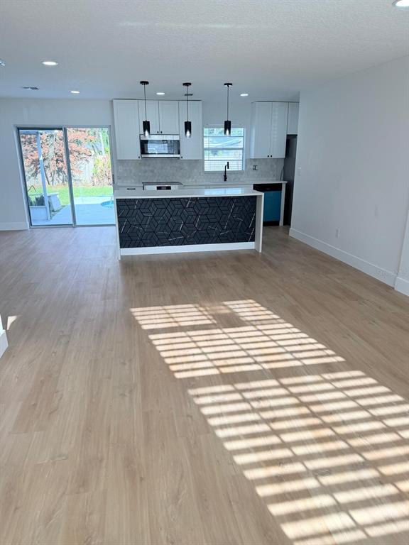 A modern kitchen features white cabinets, a geometric-patterned island, and light wood-look flooring — 115 MEADOWFIELD LANE, LONGWOOD, FL