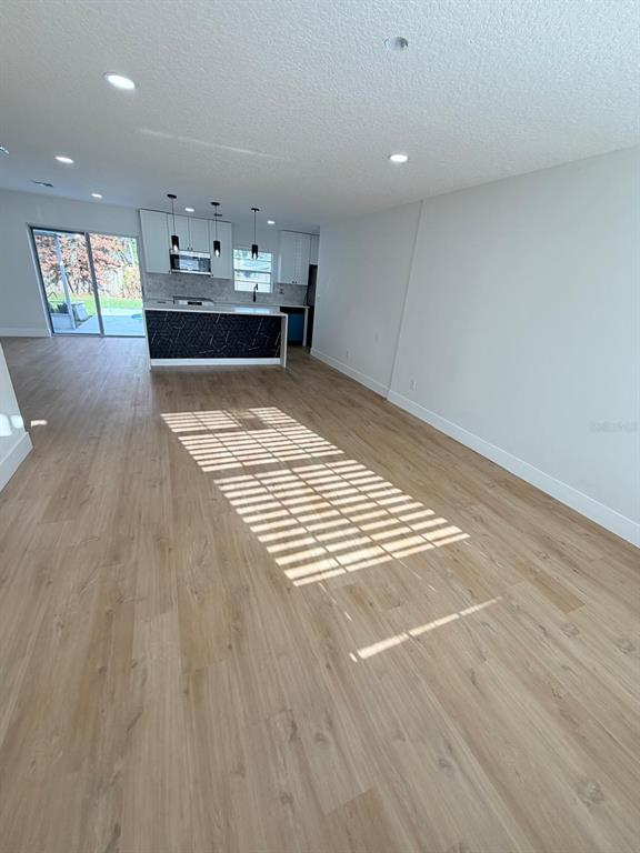 An open-concept living area features light wood-look flooring, recessed lighting, and a kitchen island — 115 MEADOWFIELD LANE, LONGWOOD, FL