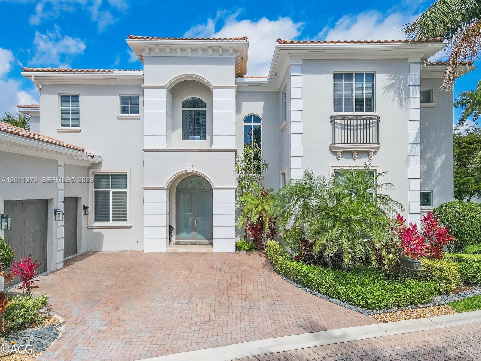 A two-story house with a light-colored stucco exterior, arched entryway, and a brick driveway — 1480 Windjammer Way, Hollywood FL 33019, HOLLYWOOD, FL