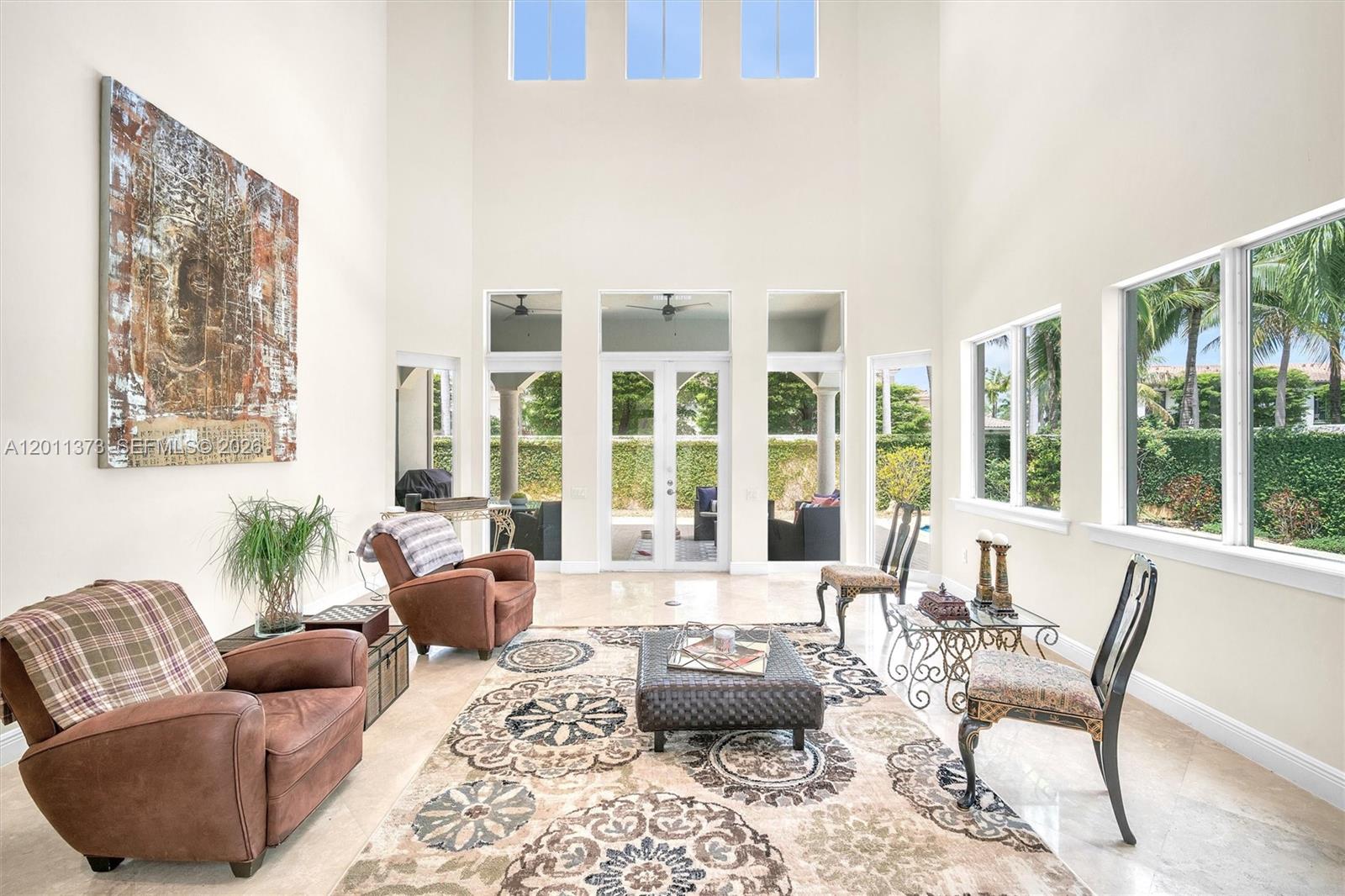 A spacious living room features high ceilings, large windows, tile floors, and a patterned area rug — 1480 Windjammer Way, Hollywood FL 33019, HOLLYWOOD, FL