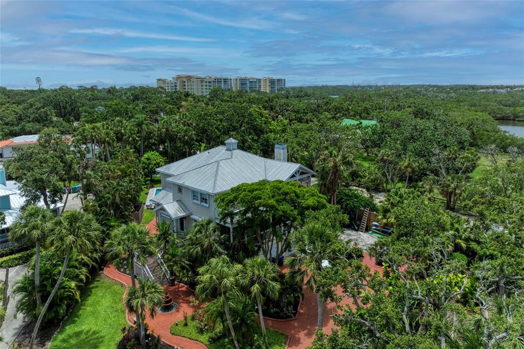 An aerial view shows a two-story house with a metal roof surrounded by lush trees — 8963 FISHERMENS BAY DRIVE, SARASOTA, FL