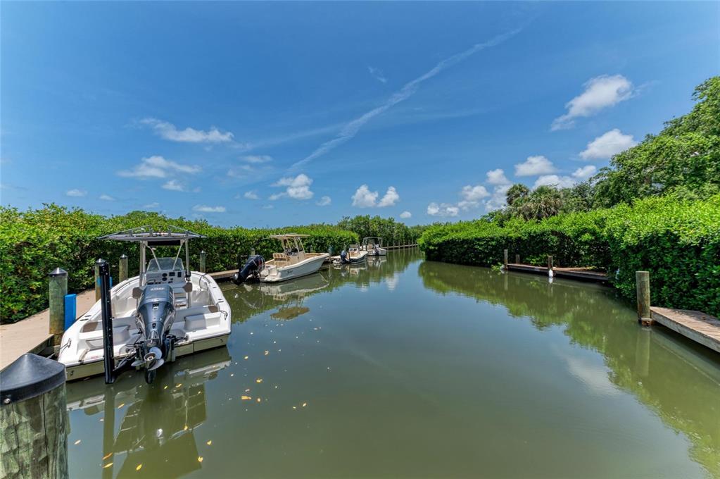 A narrow canal lined with lush green vegetation features several docked motorboats under a blue sky — 8963 FISHERMENS BAY DRIVE, SARASOTA, FL