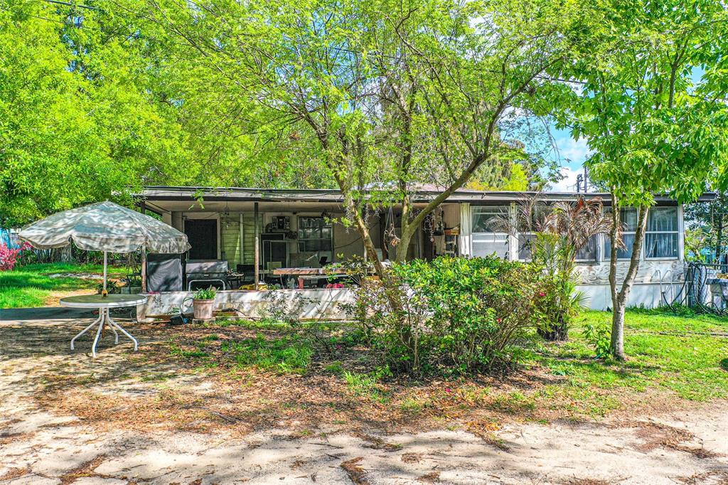 A single-story mobile home with a covered porch sits in a tree-shaded, sandy yard — 100 N SELF AVENUE, AVON PARK, FL