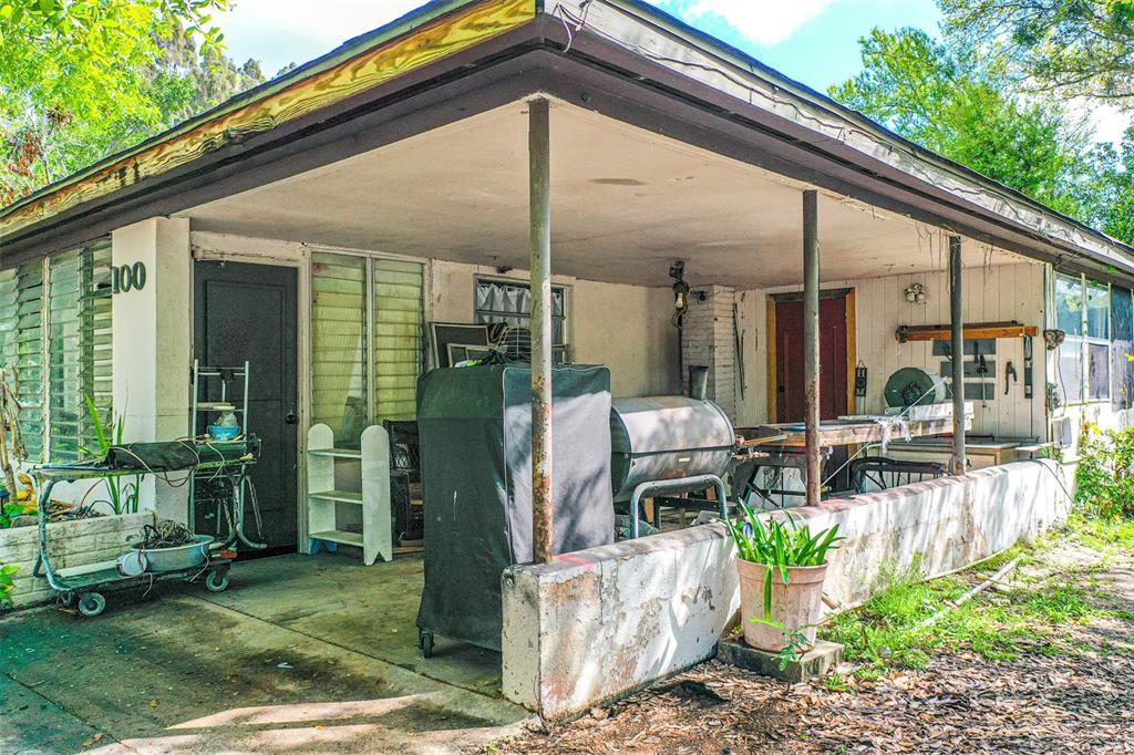 A covered concrete porch features a brick wall, metal support posts, and various outdoor items — 100 N SELF AVENUE, AVON PARK, FL