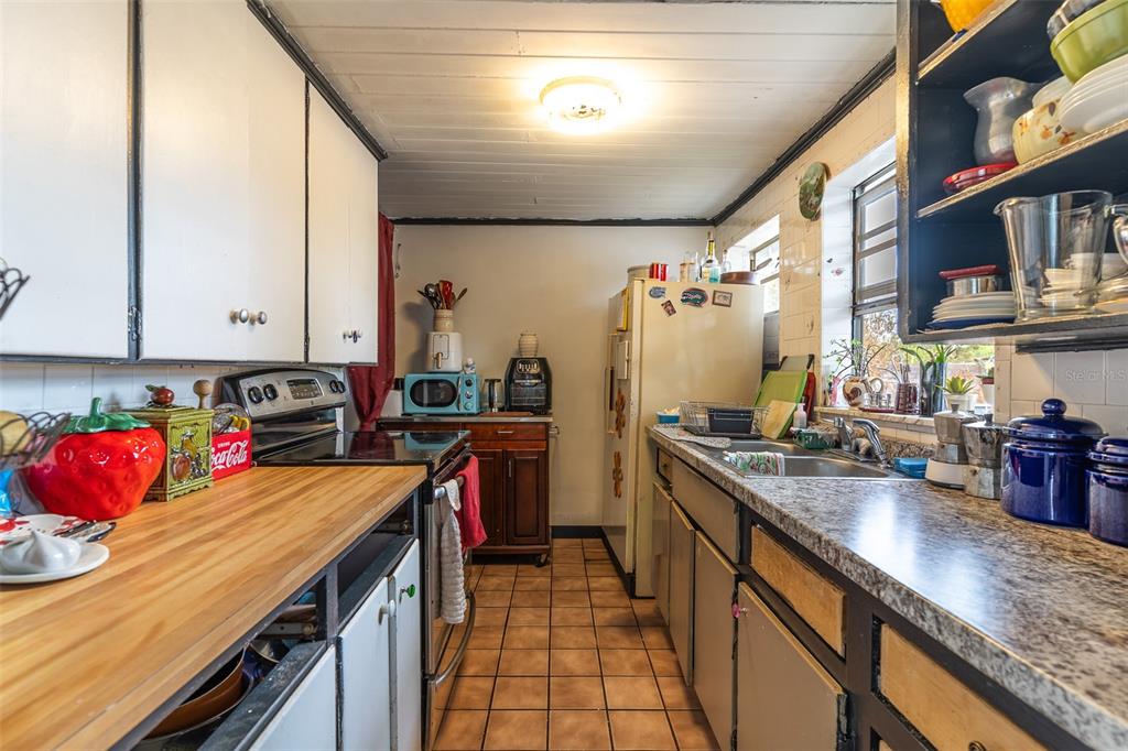 A kitchen features white cabinets, a wood countertop, a stainless stove, and a tiled floor — 100 N SELF AVENUE, AVON PARK, FL
