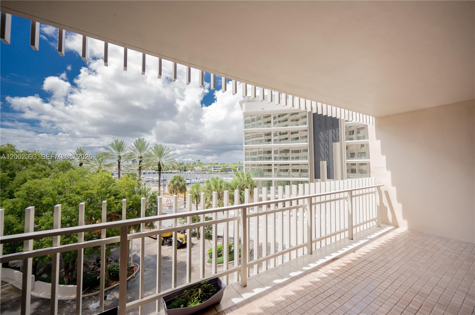 A balcony with a white railing overlooks a parking area, palm trees, and a waterway — 3 Grove Isle Dr # C308, Miami FL 33133, MIAMI, FL