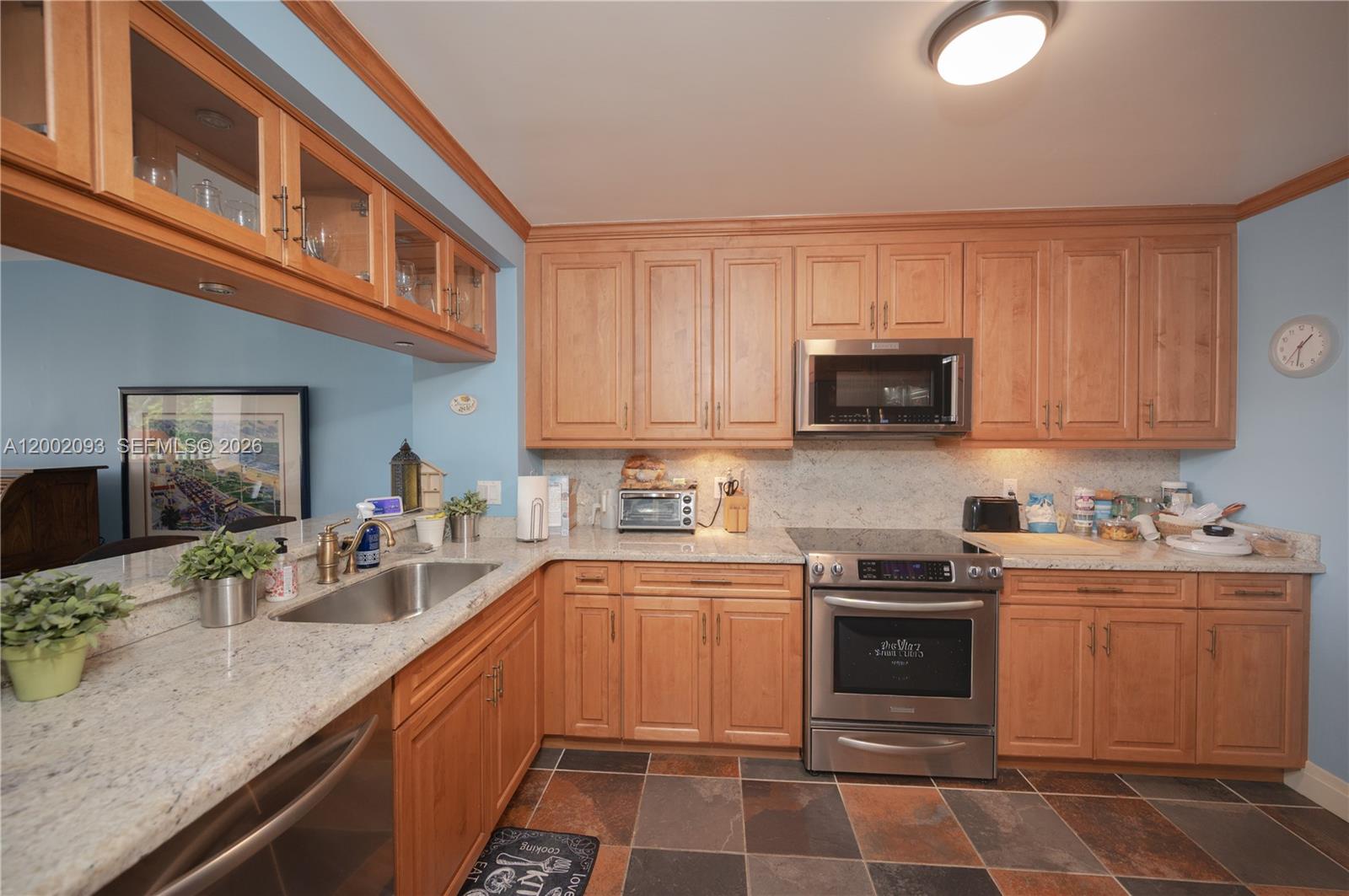 A kitchen features light wood cabinets, granite countertops, stainless steel appliances, and slate tile flooring — 3 Grove Isle Dr # C308, Miami FL 33133, MIAMI, FL