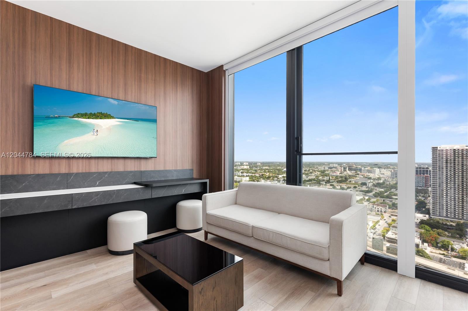 A modern living room features wood-paneled walls, a white sofa, and floor-to-ceiling windows — 20 NE 11th # 2905, Miami FL 33132, MIAMI, FL