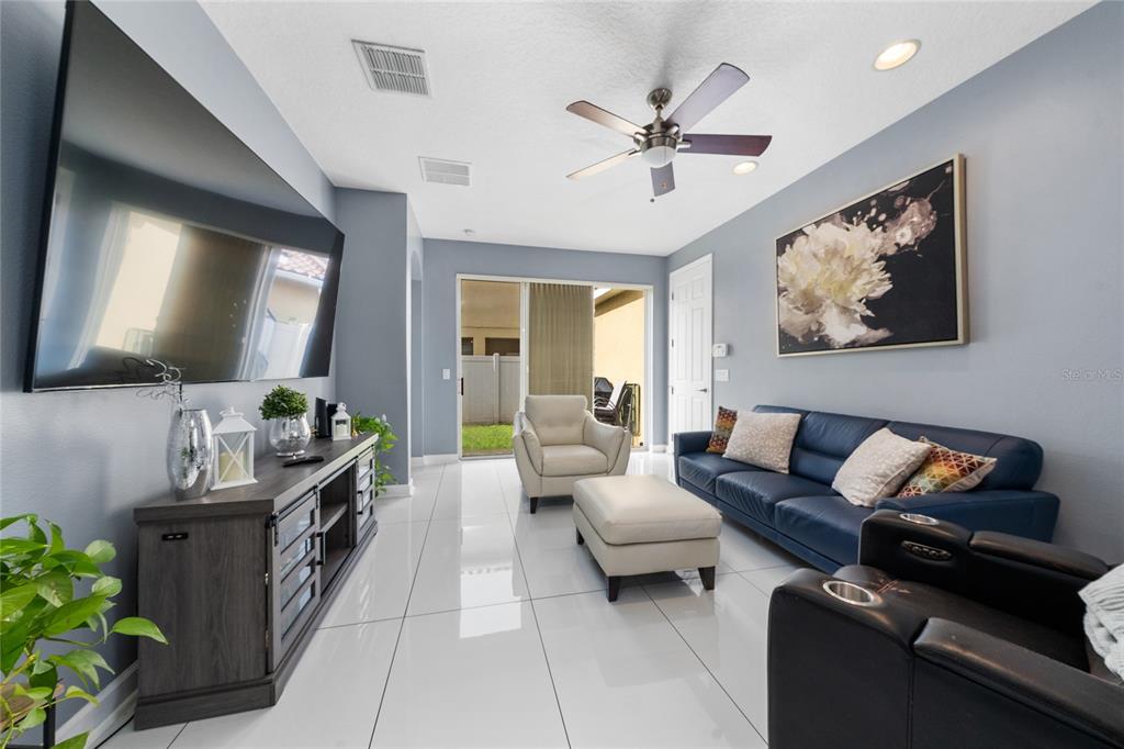 A living room features a blue sofa, white armchair, ottoman, and large wall-mounted television — 2680 DOLFINO COURT, ST CLOUD, FL