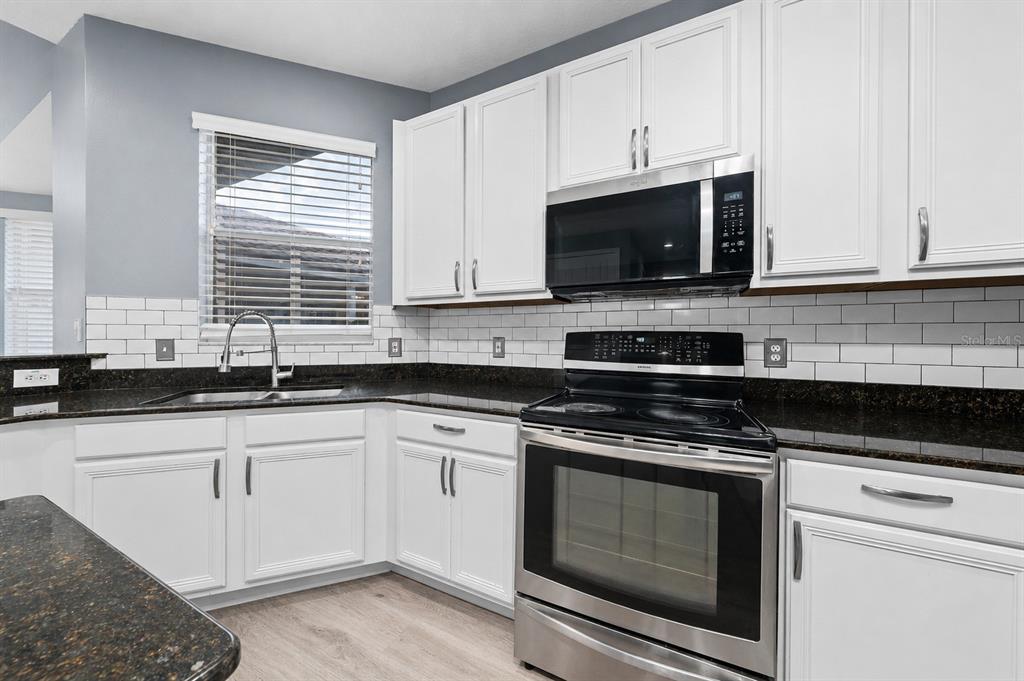 A kitchen with white cabinets, dark granite countertops, stainless steel appliances, and a subway tile backsplash — 2680 DOLFINO COURT, ST CLOUD, FL