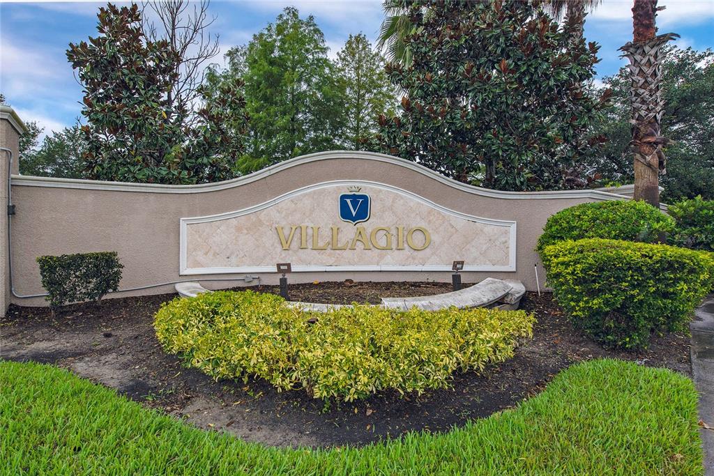 A beige stucco monument sign for Villagio stands in a landscaped garden bed — 2680 DOLFINO COURT, ST CLOUD, FL