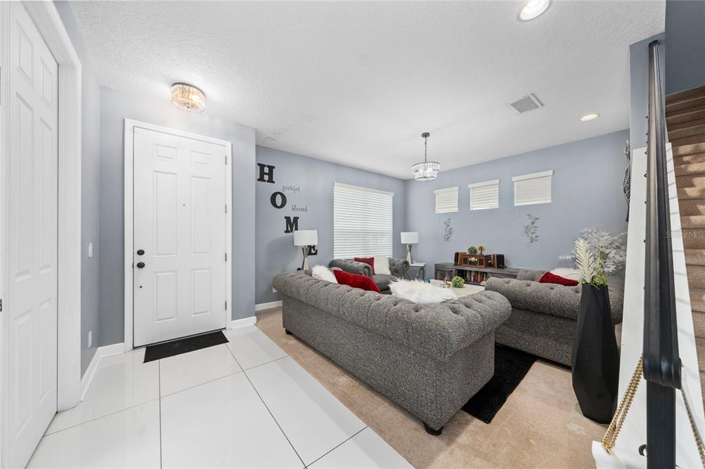 A living room features gray walls, a tufted sofa, tile flooring, and a staircase — 2680 DOLFINO COURT, ST CLOUD, FL