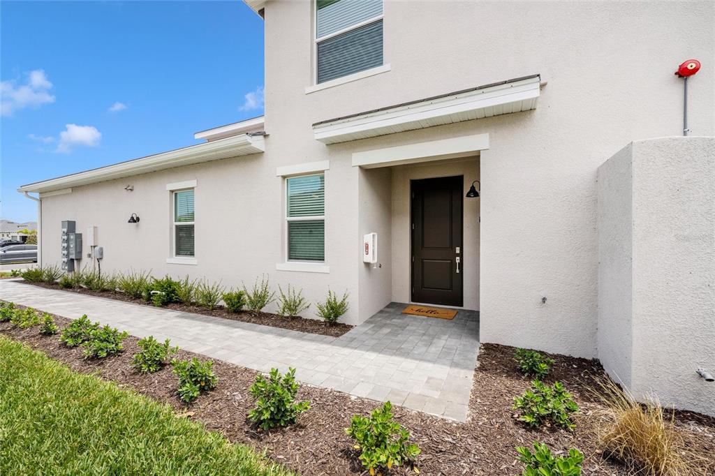 A paved walkway leads to the dark front door of a light-colored stucco townhouse — 12967 BLACKBERRY COURT UNIT 102, VENICE, FL