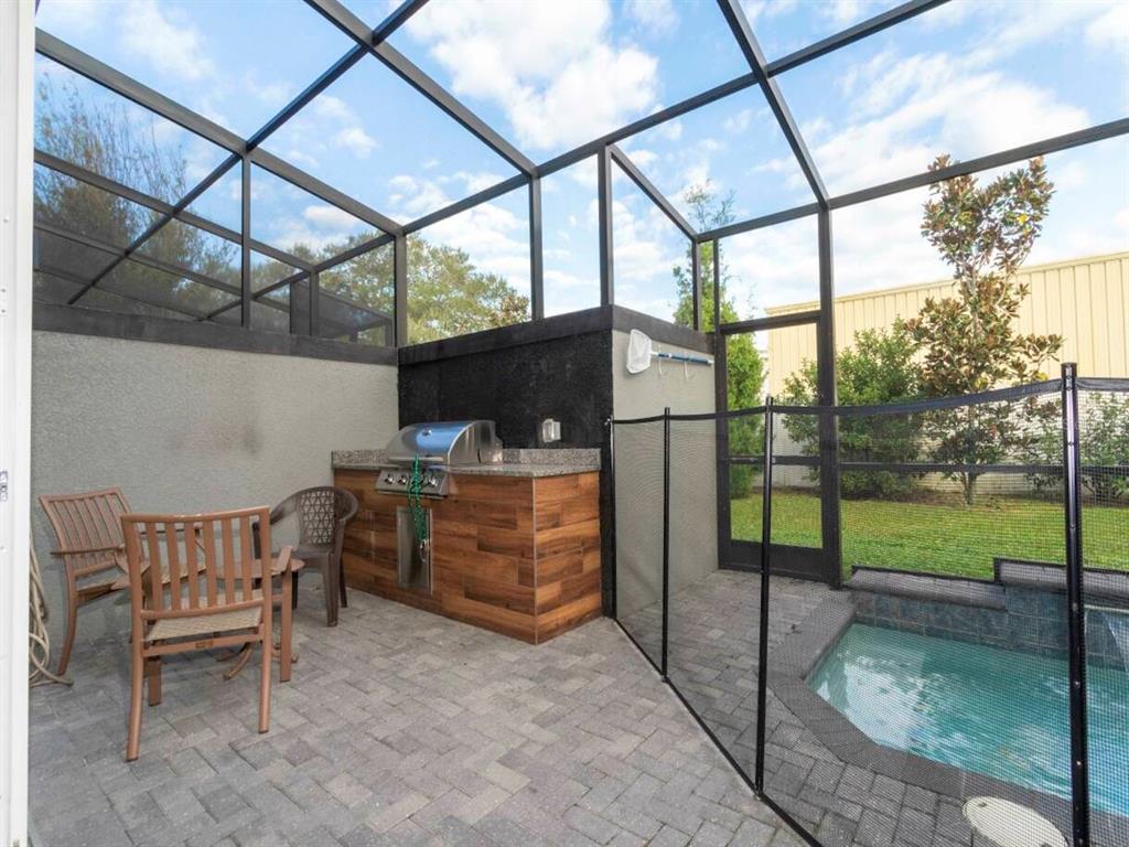 An outdoor kitchen with a grill sits on a patio next to a screened pool — 4425 LE REVE COURT, KISSIMMEE, FL
