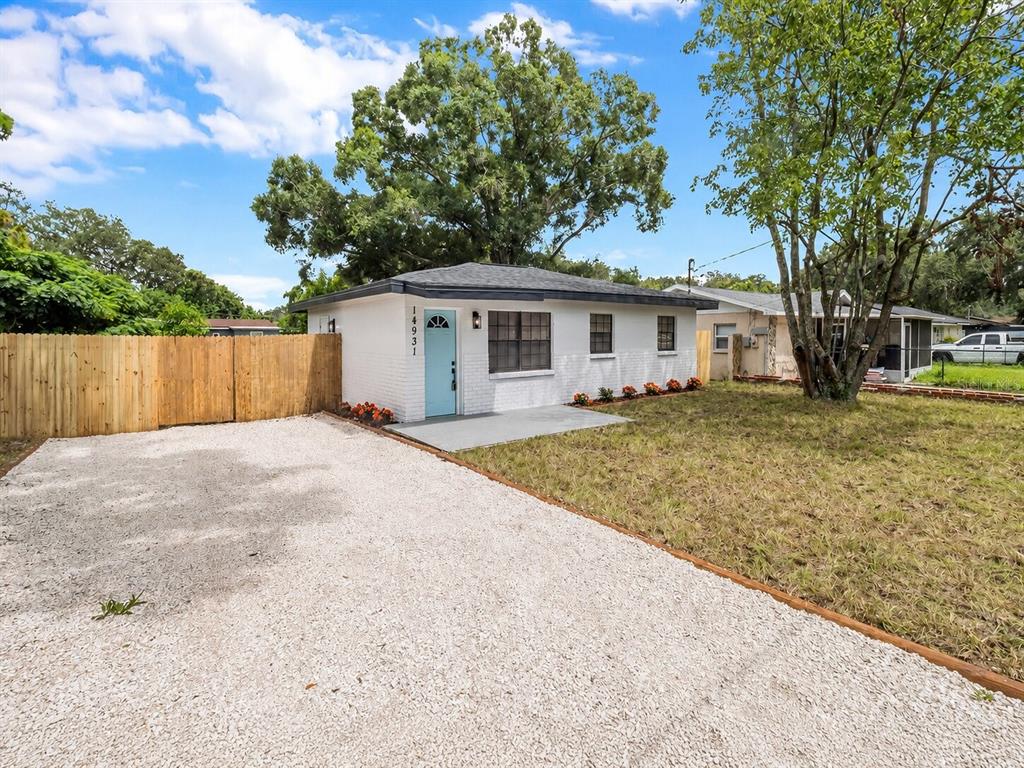 A white brick house with a light blue front door and a gravel driveway — 14931 FISHER ROAD, TAMPA, FL