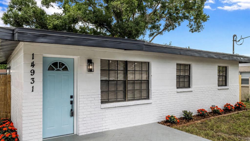 A white brick house exterior features a light blue front door and a paved patio — 14931 FISHER ROAD, TAMPA, FL