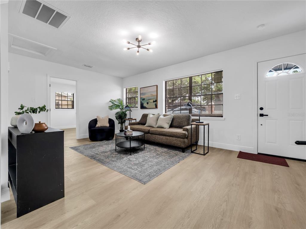 A living room features light wood flooring, a brown sofa, a dark rug, and a front door — 14931 FISHER ROAD, TAMPA, FL